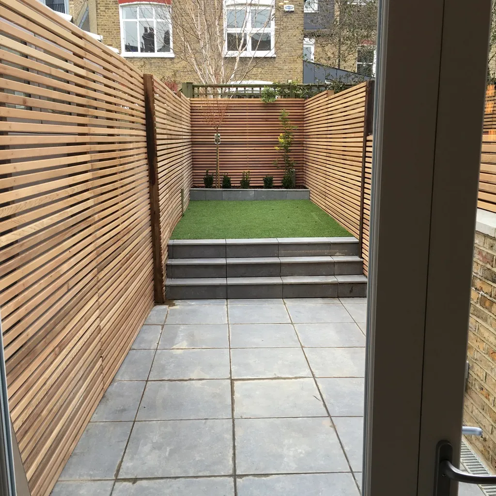 Landscaped rear garden with cedar slatted fencing, paving and steps up to lawn, for the ground-floor Clapham flat
