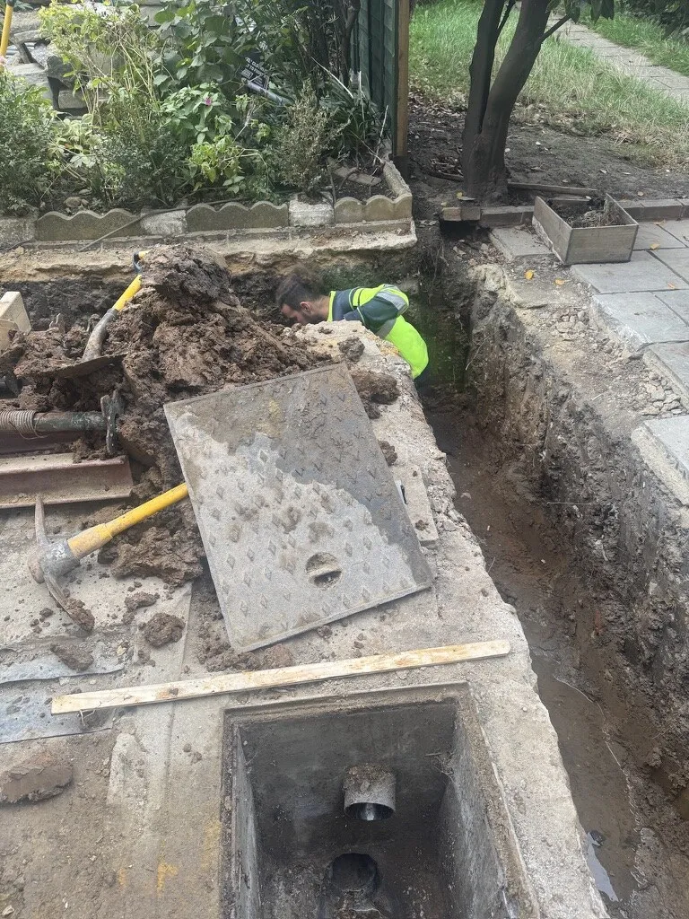 Groundworker excavating and tracing the existing drain run beside the rear garden of an Earlsfield Victorian terrace