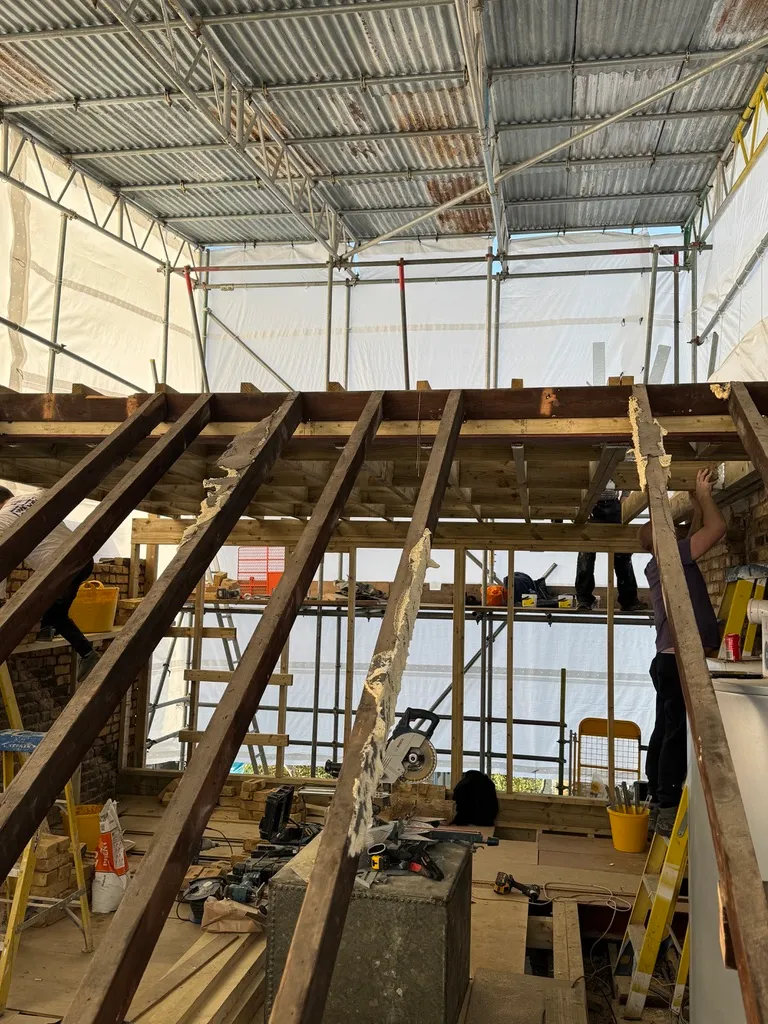 New timber floor structure being built over the original rafters beneath a temporary scaffold roof